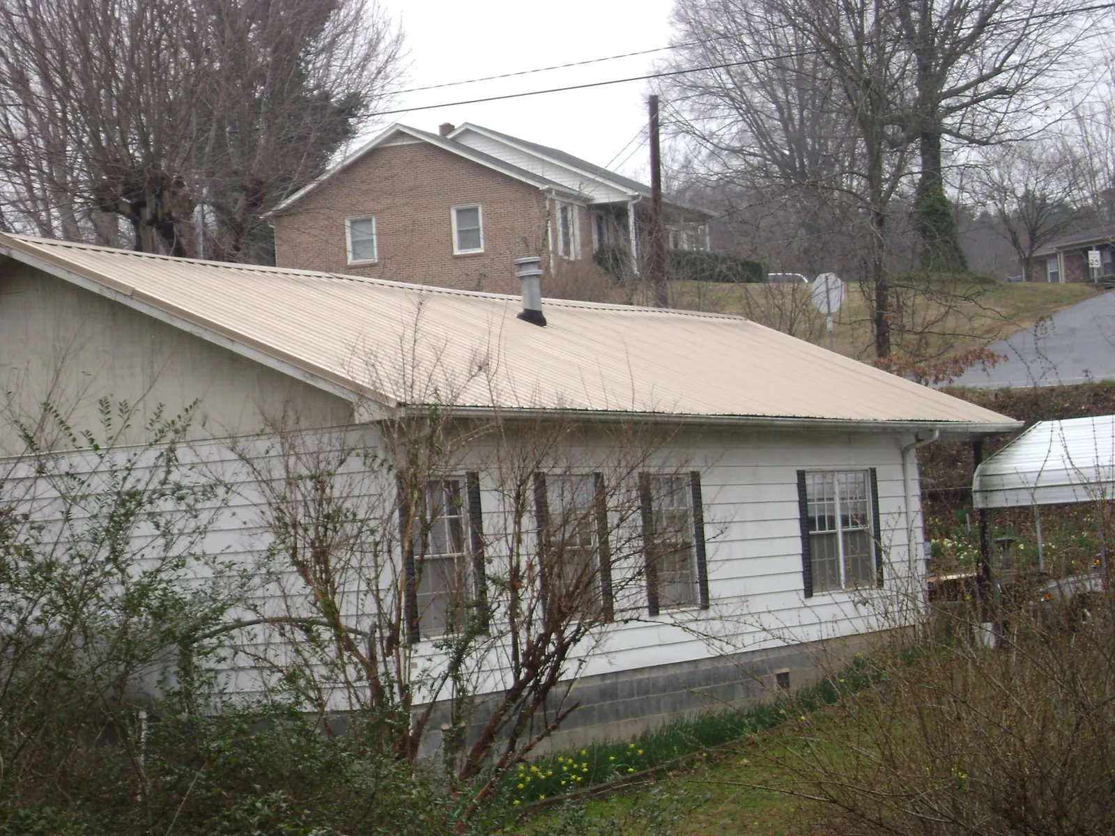 Tan metal roof on a white sided house set into a hillside — Commercial Roofing by Roofing Brothers in Sutton